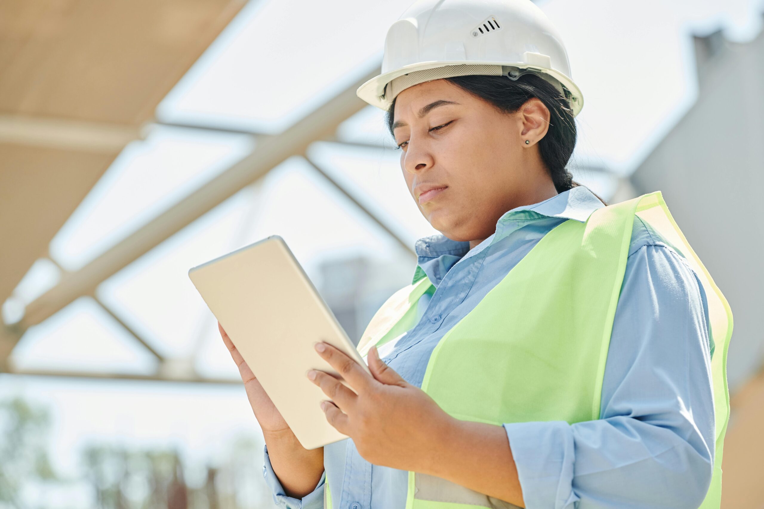 Confident female engineer in hard hat using a tablet computer at an outdoor construction site.